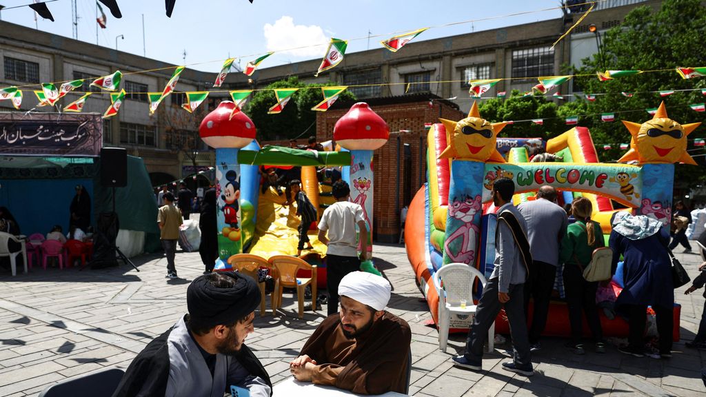 Dos clérigos conversan en un bazar de Teherán frente a unos castillos hinchables para niños durante el alto el fuego.