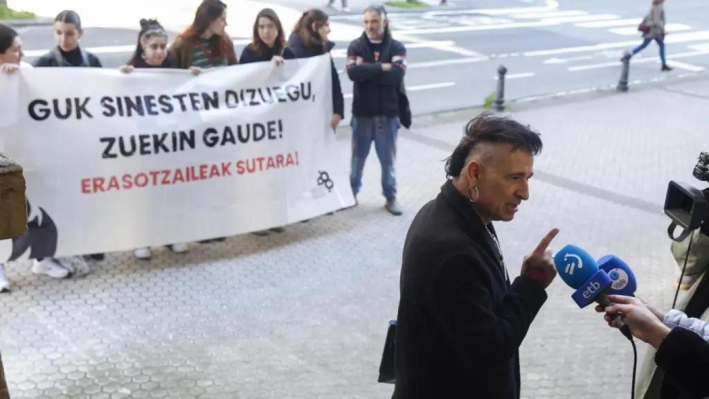 Jon Perurena atiende a los medios durante el juicio, frente a una pancarta en defensa de sus denunciantes.