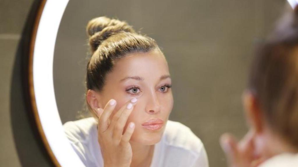 Mujer aplicándose corrector frente al espejo.