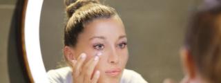 Mujer aplicándose corrector frente al espejo.