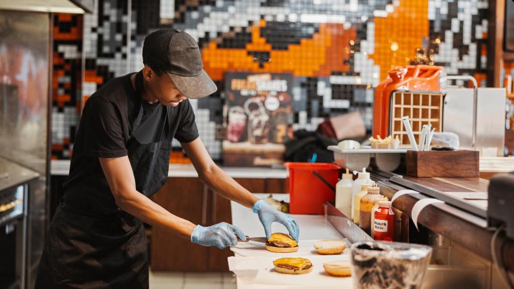Un trabajador preparando unas hamburguesas en una cadena de comida rápida.