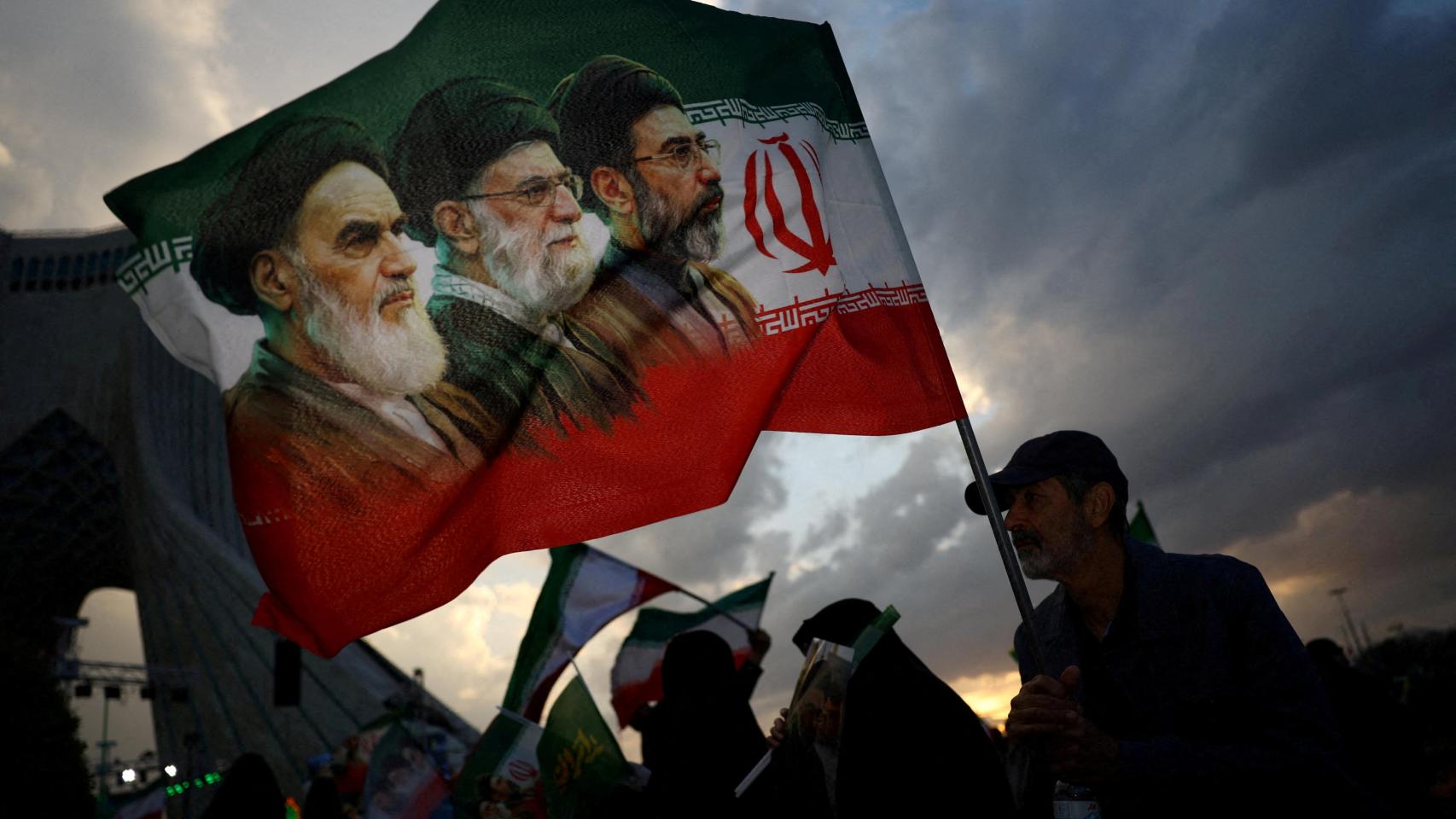 Un hombre sostiene una bandera con una imagen del fallecido líder de la Revolución Islámica, el ayatolá Ruhollah Jomeini, del fallecido ayatolá Ali Jamenei, y del nuevo líder supremo, Mojtaba Jamenei.