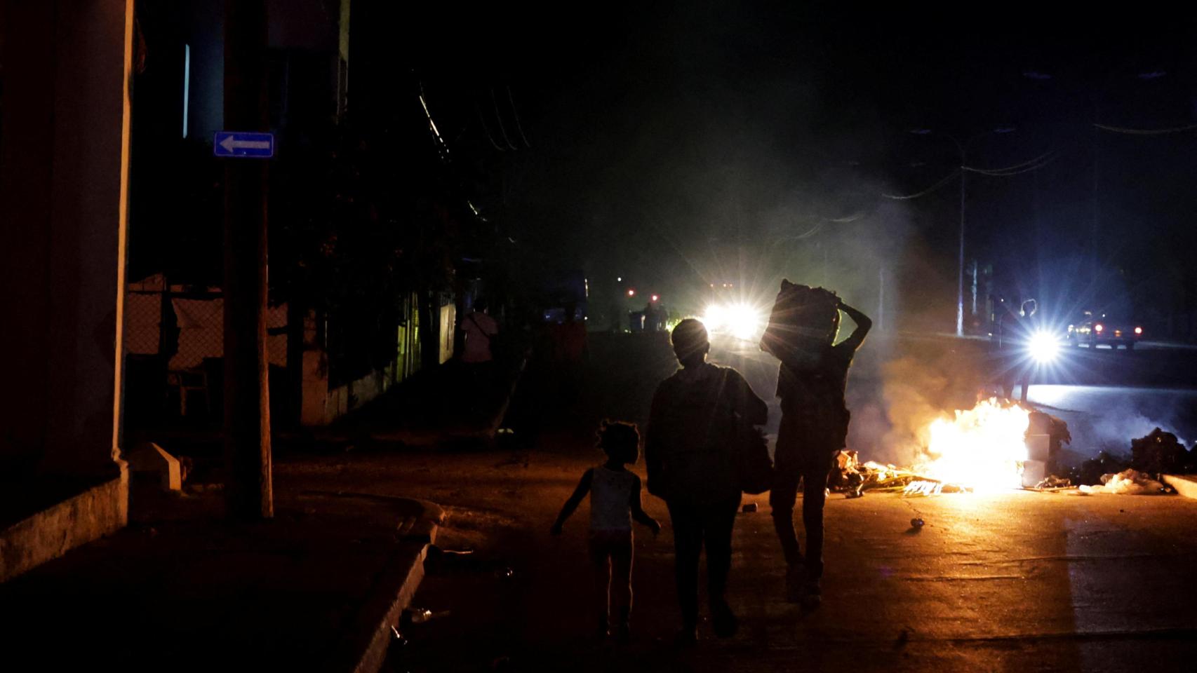 Varias personas caminan junto a basura incendiada en medio de una calle durante una protesta contra los frecuentes cortes de luz.