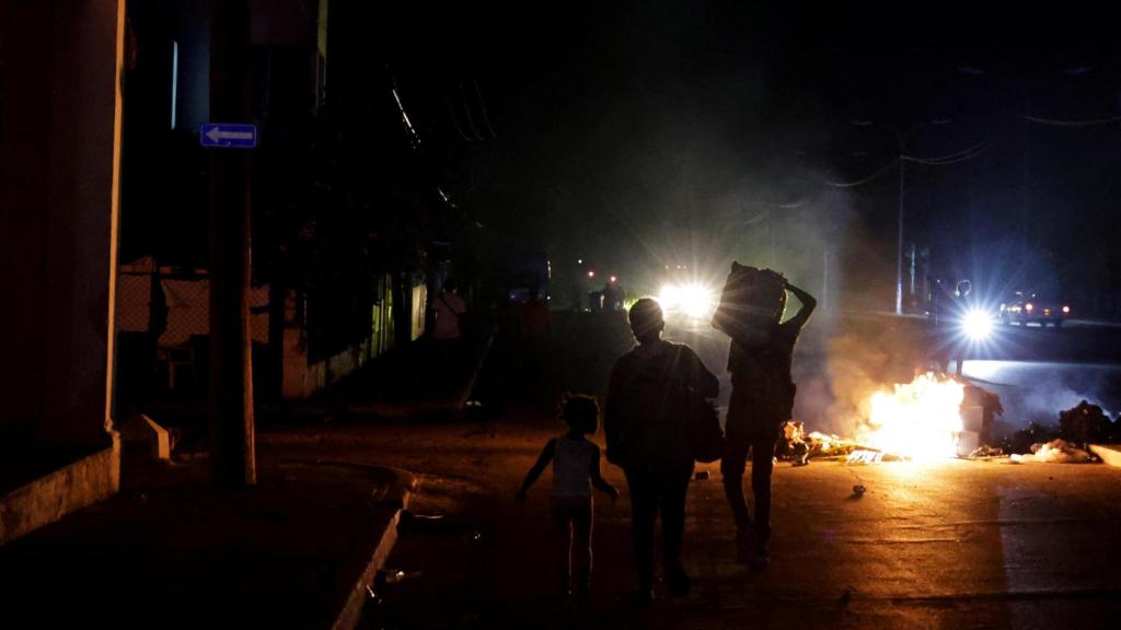 Varias personas caminan junto a basura incendiada en medio de una calle durante una protesta contra los frecuentes cortes de luz.