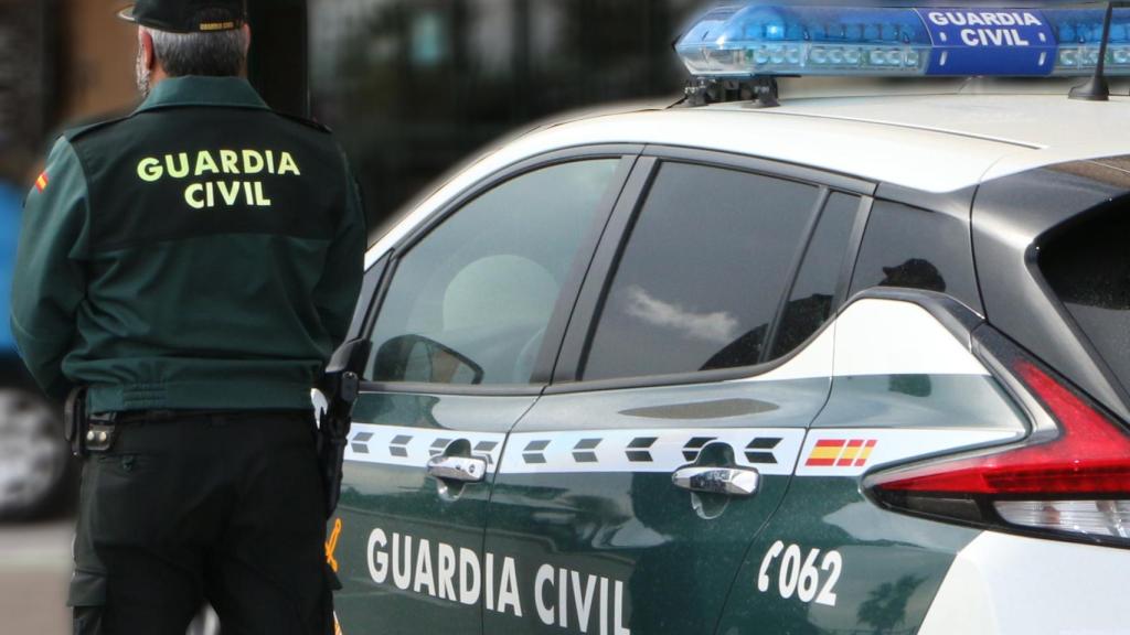 Un agente de la Guardia Civil, de espaldas, de pie junto a un vehículo oficial. EE