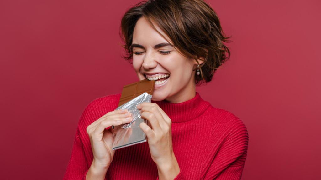 Joven emocionada comiendo barra de chocolate.