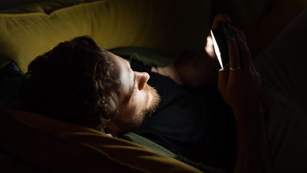 Un hombre mira el móvil antes de dormir.