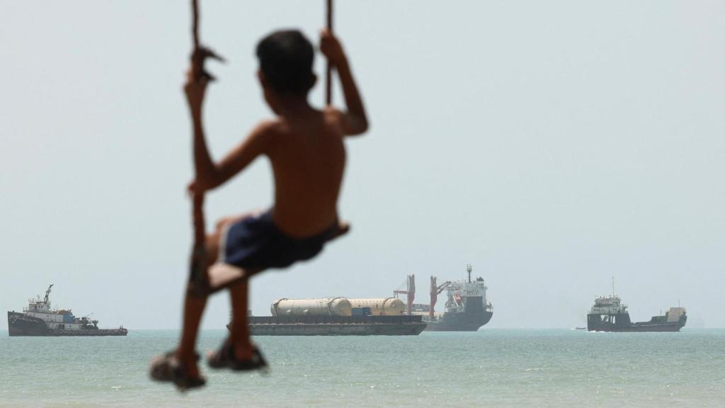 Un niño juega en la playa, con embarcaciones en el estrecho de Ormuz visibles cerca de la playa de Bandar Abás.