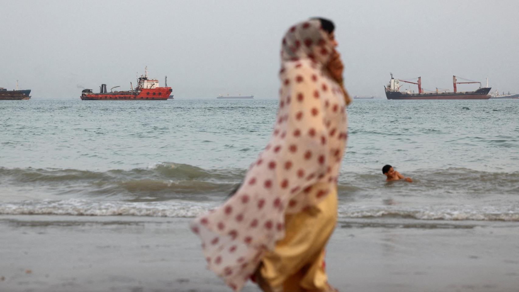 La gente camina por la playa, con embarcaciones visibles en el estrecho de Ormuz cerca de la playa de Bandar Abbas.