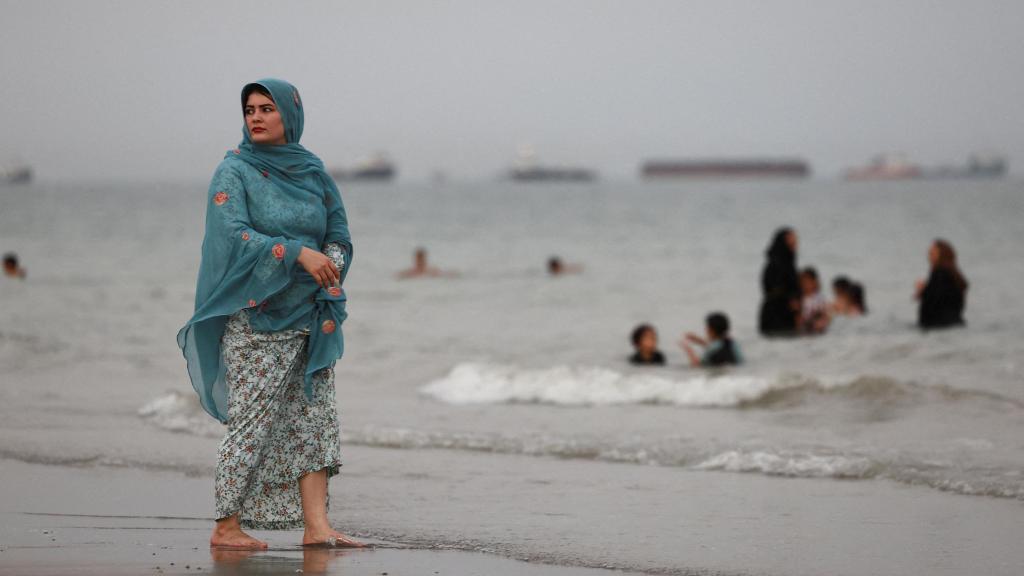 Mujer iraní pasea por la playa de Bandar Abbas mientras los barcos siguen atrapados dentro del Golfo Pérsico.