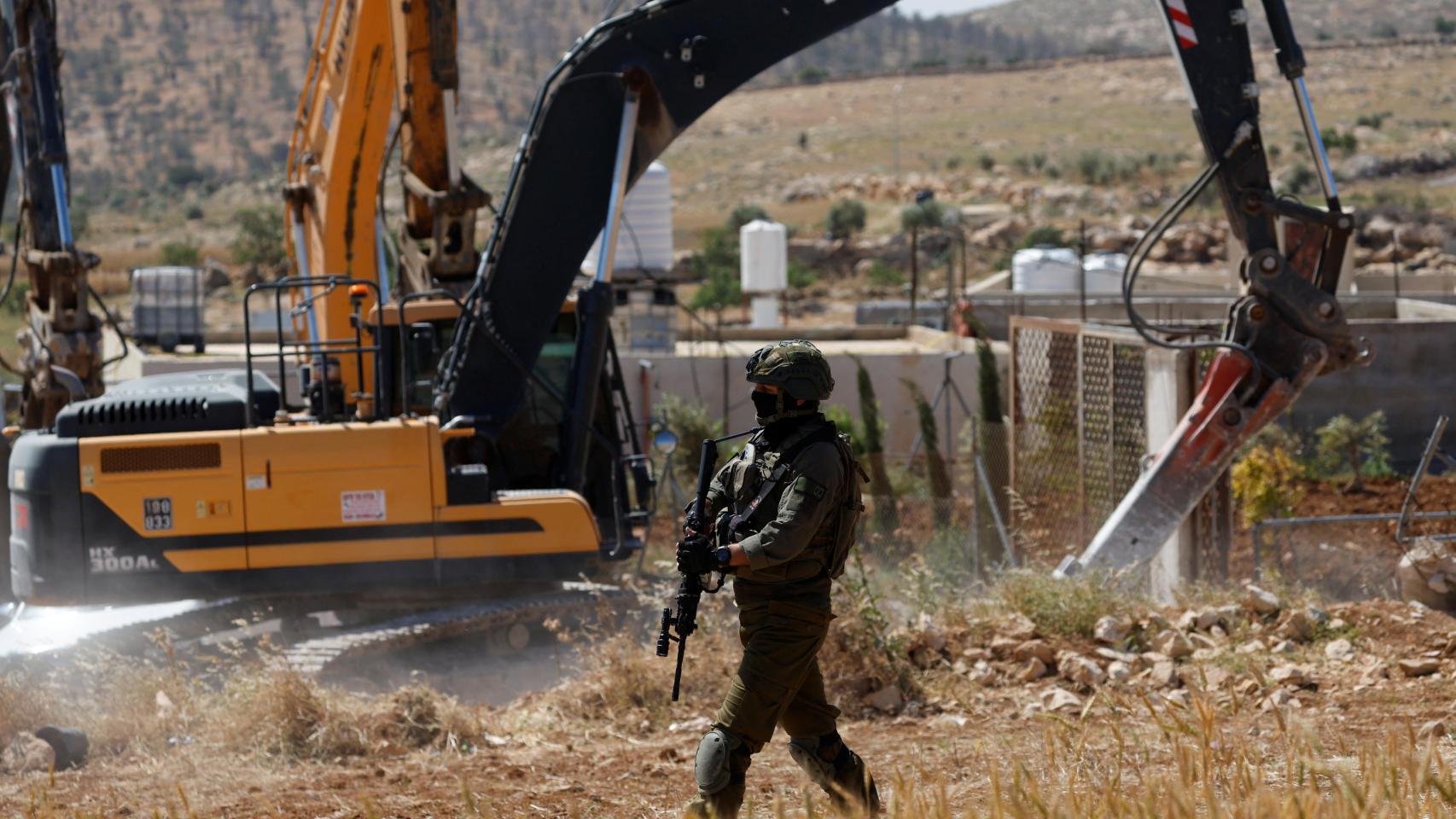 Un soldado israelí monta guardia mientras una excavadora destruye un edificio palestino cerca de Hebrón.