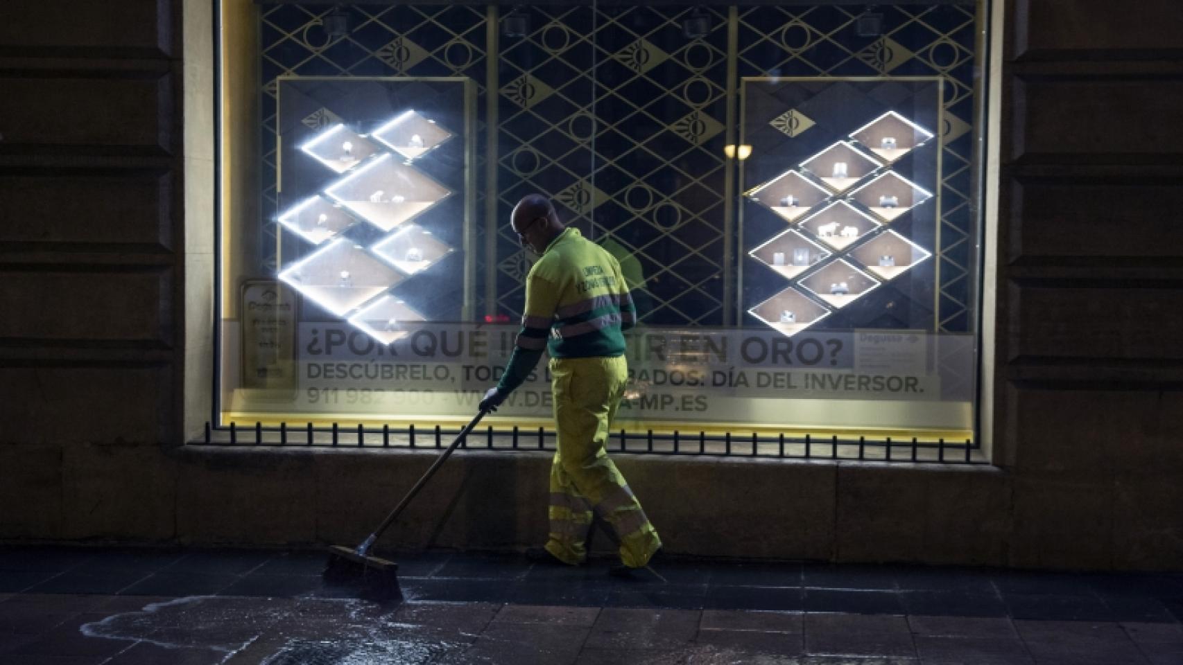 Un empleado de limpieza barriendo una calle de noche.