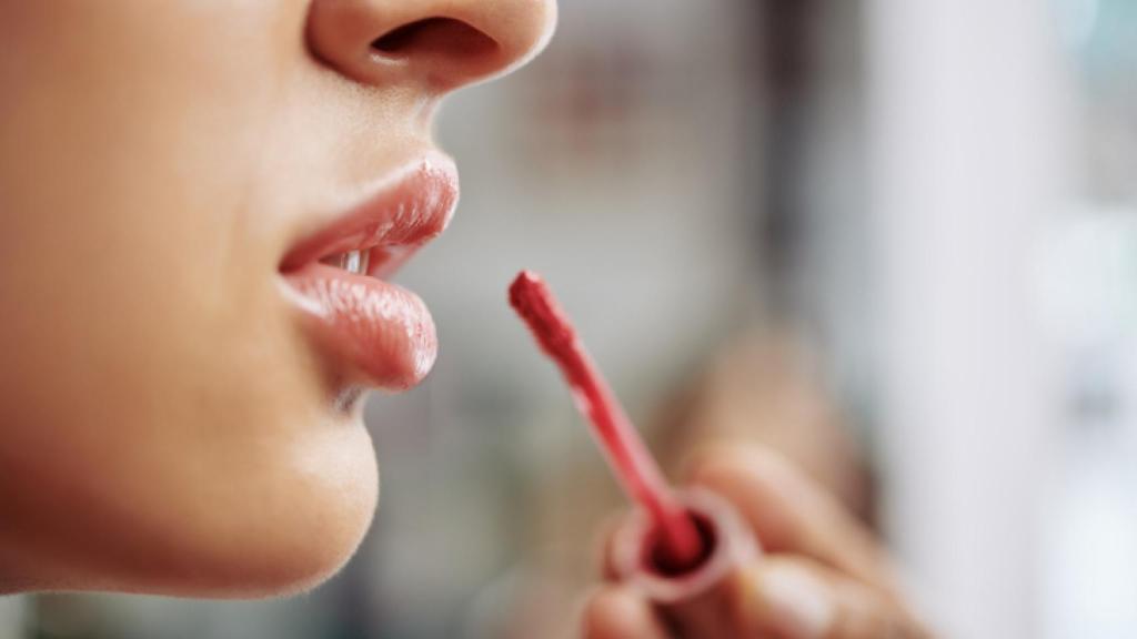 Mujer maquillándose los labios con gloss.