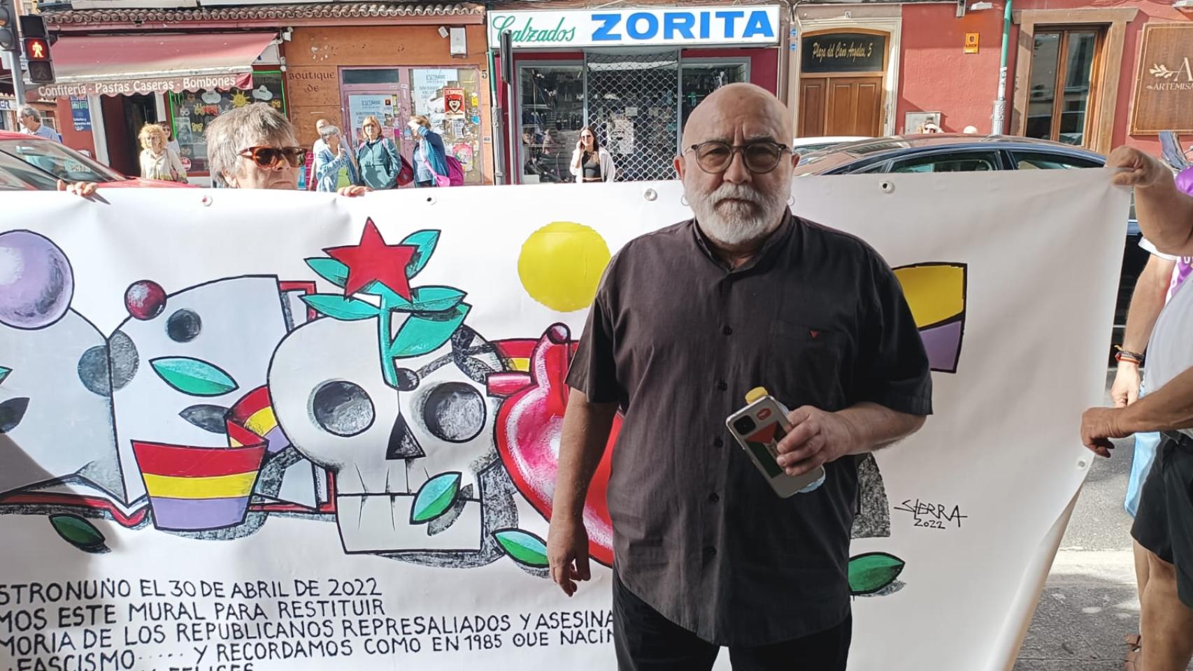 El artista Manolo Sierra posa ante una pancarta que representa el mural borrado. 