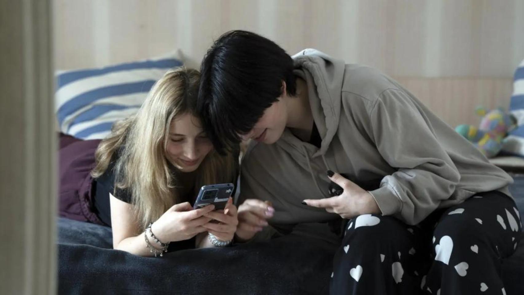 Dos adolescentes con el teléfono en una cama. 