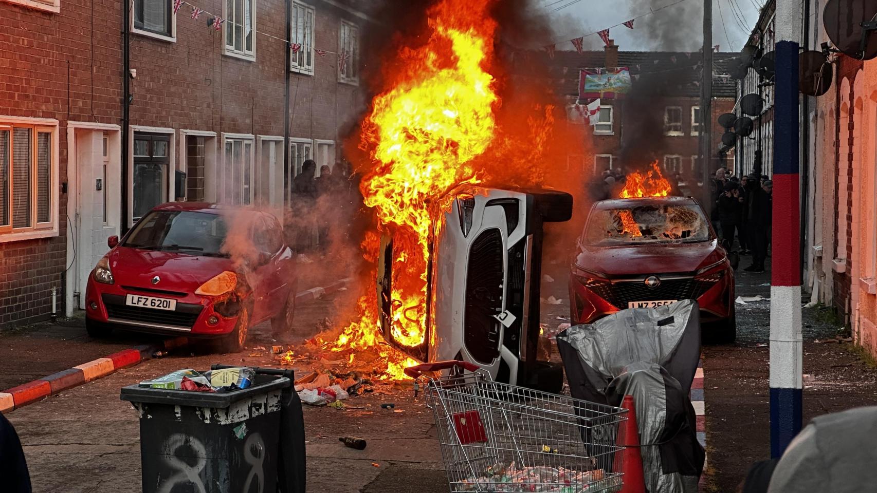 Coches ardiendo en la calle Lendrick de Belfast, tras los disturbios por el apuñalamiento de un hombre a manos de un refugiado de origen sirio.