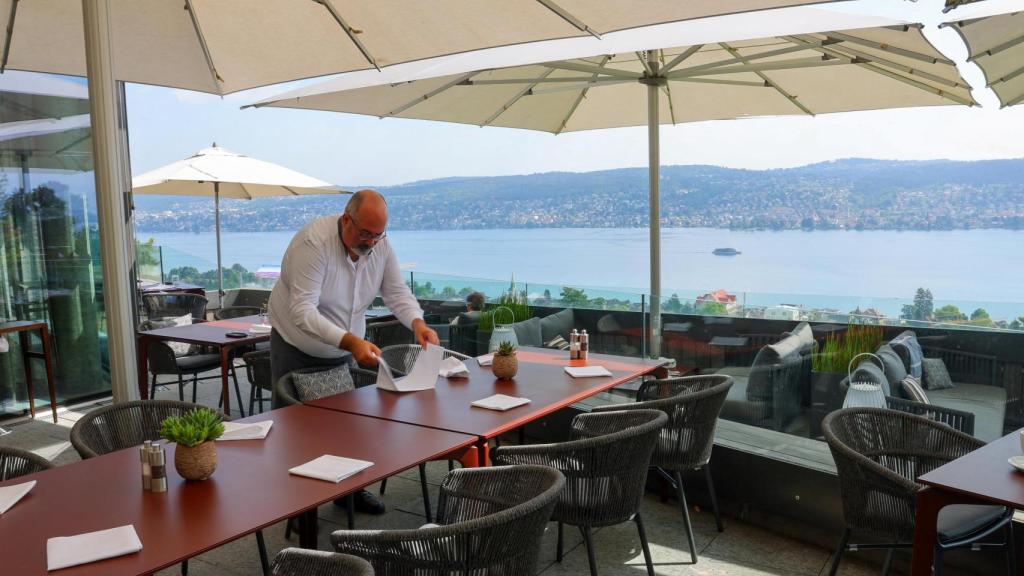 Un miembro del personal del Hotel Belvoir prepara una mesa en una terraza con vistas al lago de Zúrich en Rüschlikon.