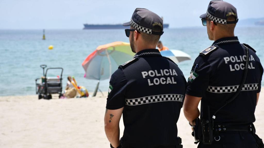 Dos policías en una playa con una sombrilla de fondo.