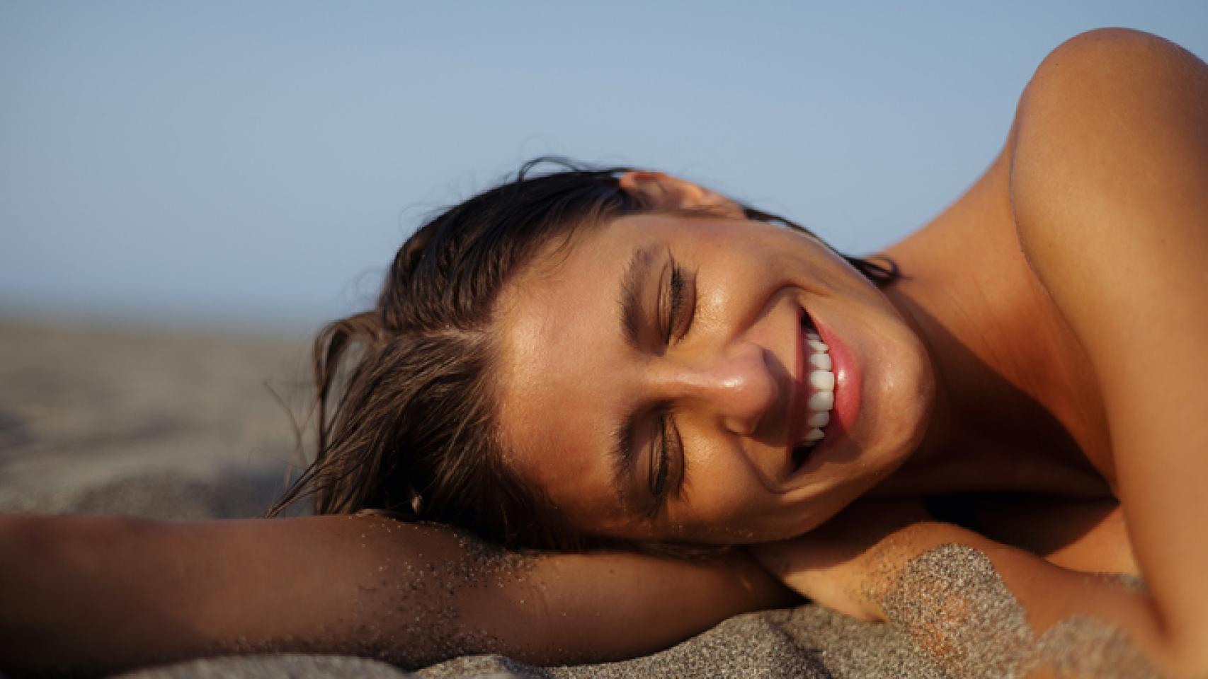 Mujer bronceada sobre la arena de la playa.