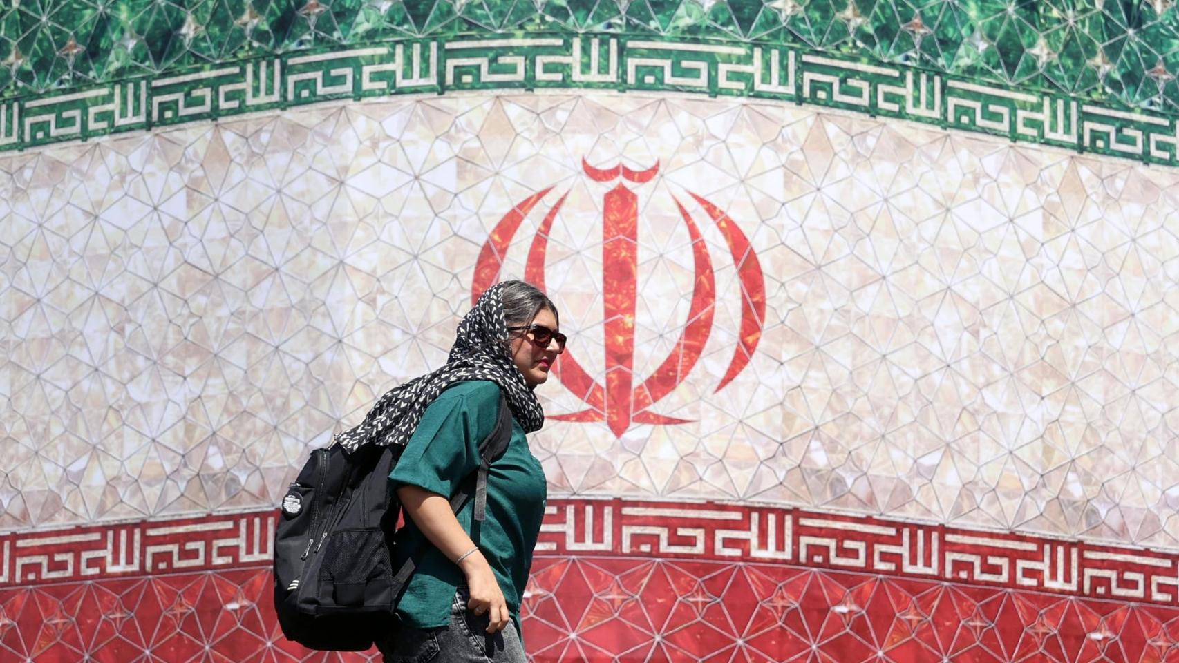 Una mujer iraní pasa junto a una valla publicitaria con la bandera nacional de Irán este domingo.