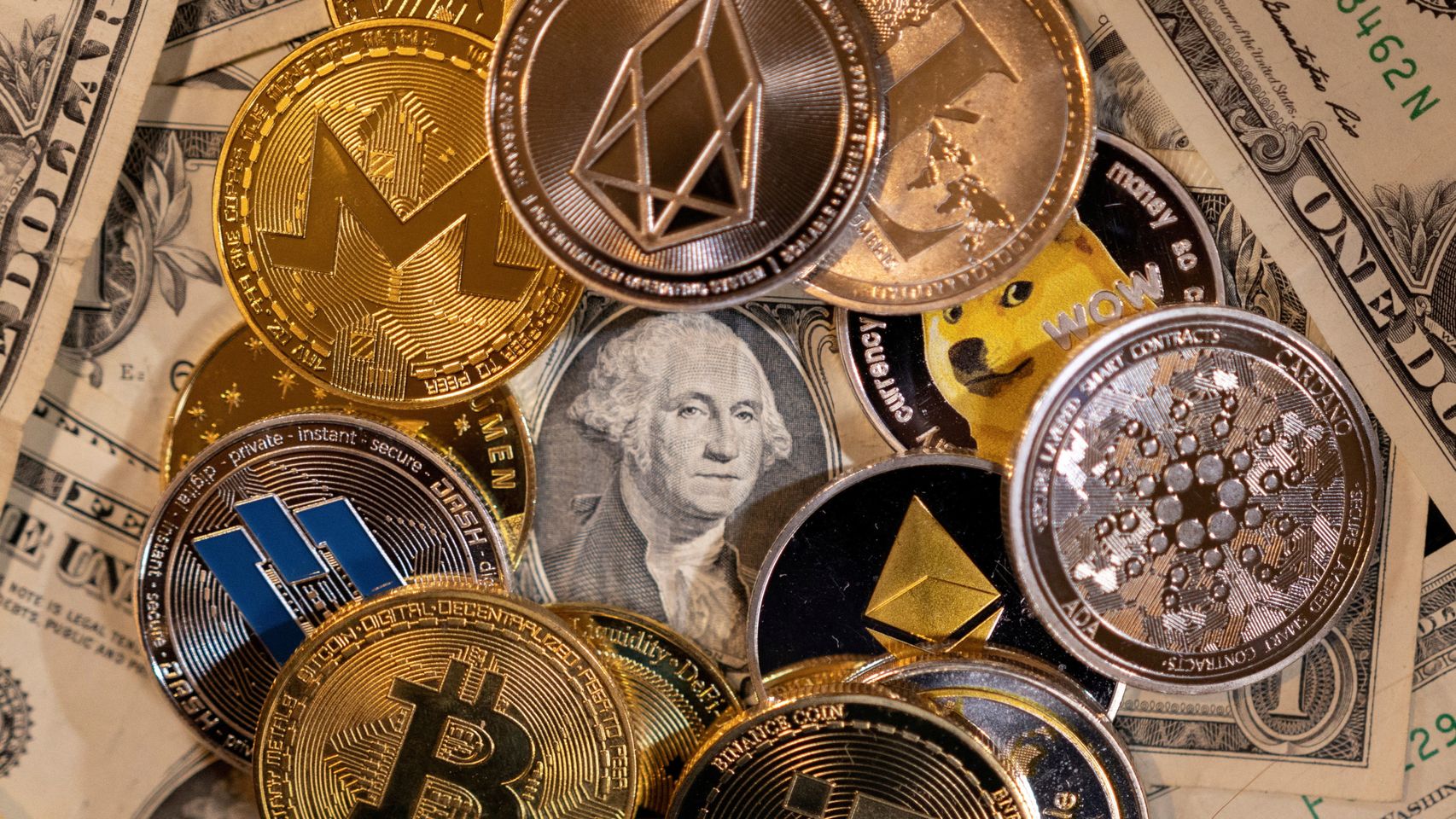 Representación física de varias criptomonedas sobre billetes de dólar.