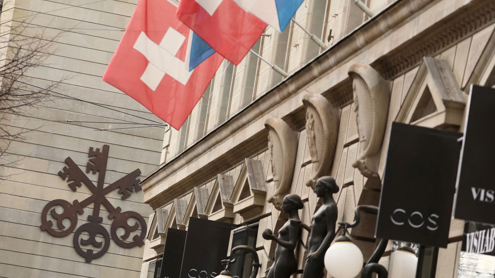 El logo de UBS en un edificio de fondo con banderas suizas.