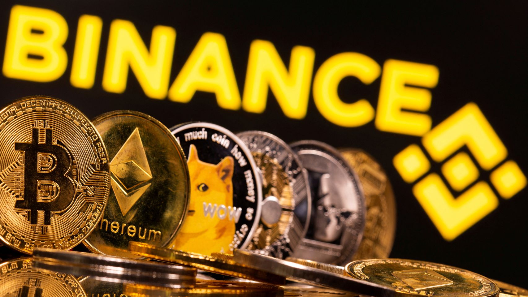 Varias representaciones físicas de criptodivisas se ven sobre el logo de Binance.