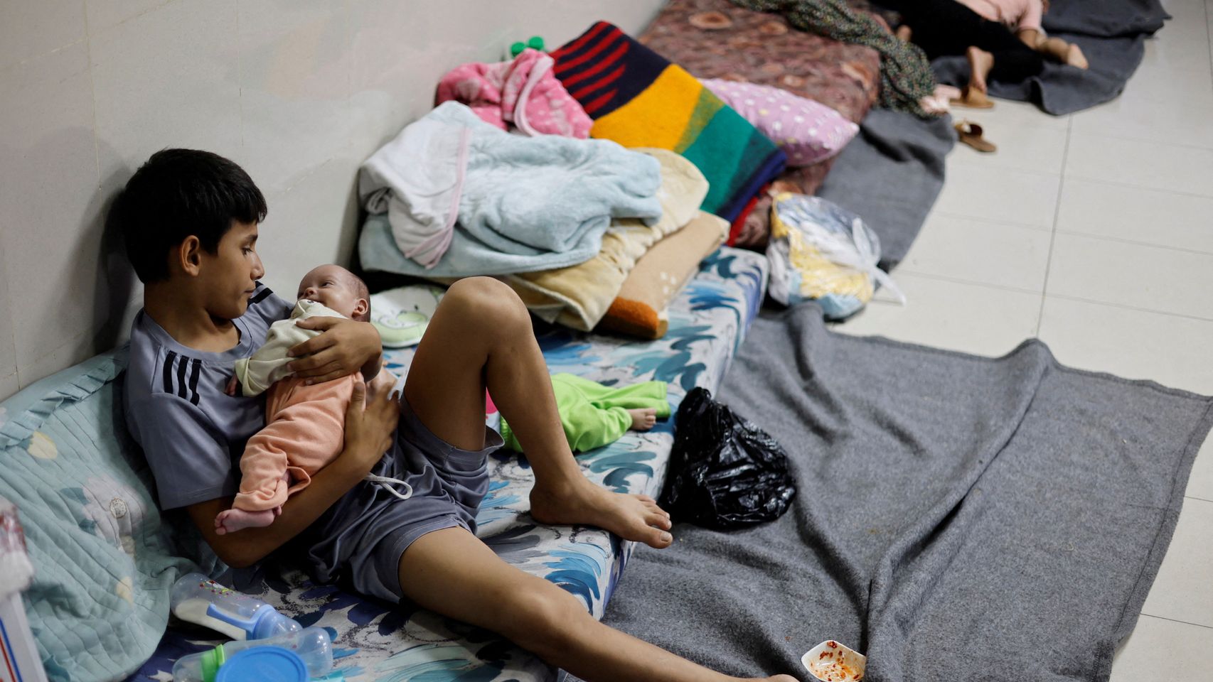 Un niño palestino desplazado cuida a sus hermanos gemelos mientras se refugian en el hospital Nasser en Khan Younis.