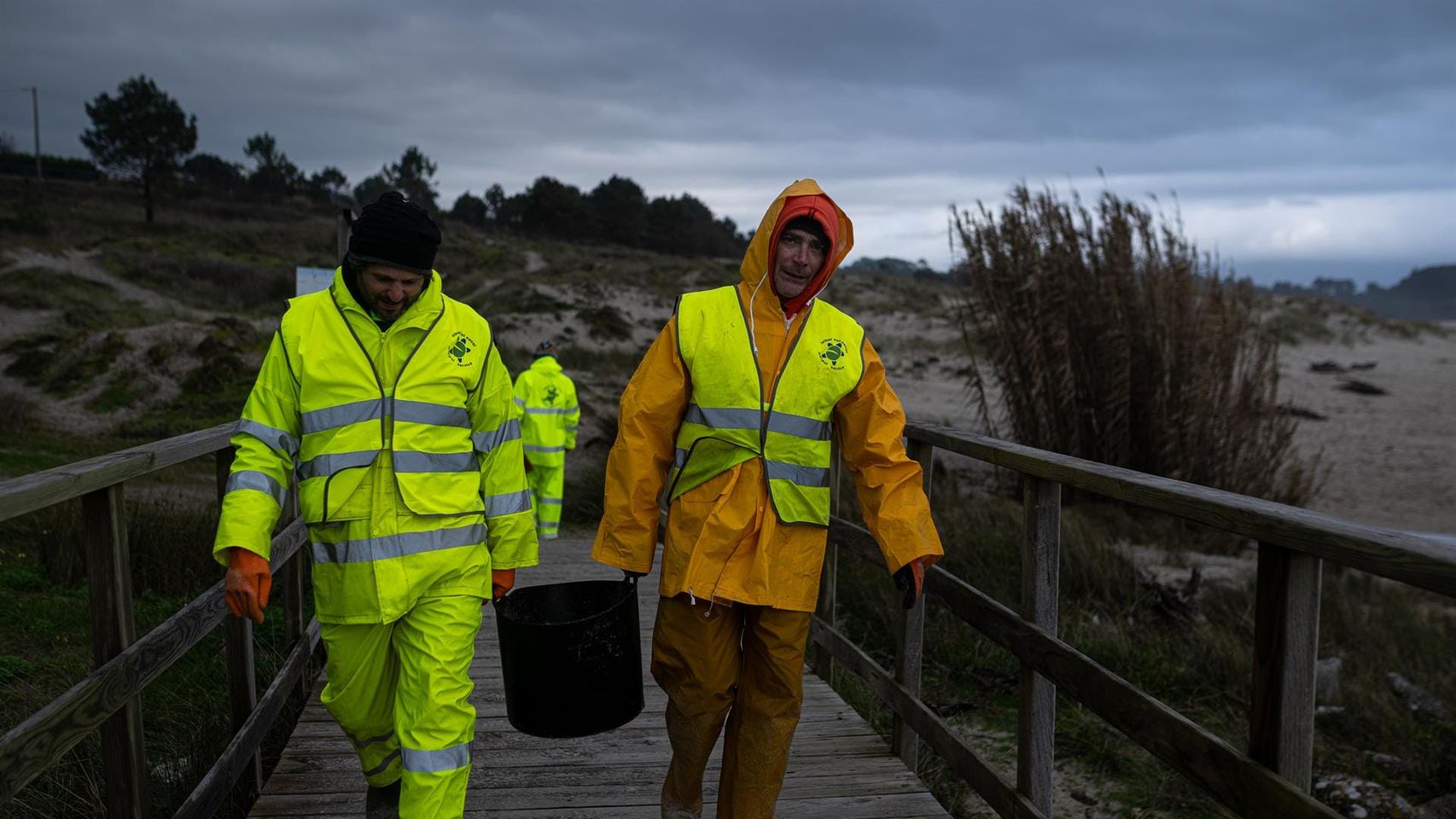 Dos hombres cargan un cubo lleno de pellets, en la playa Area Maior.