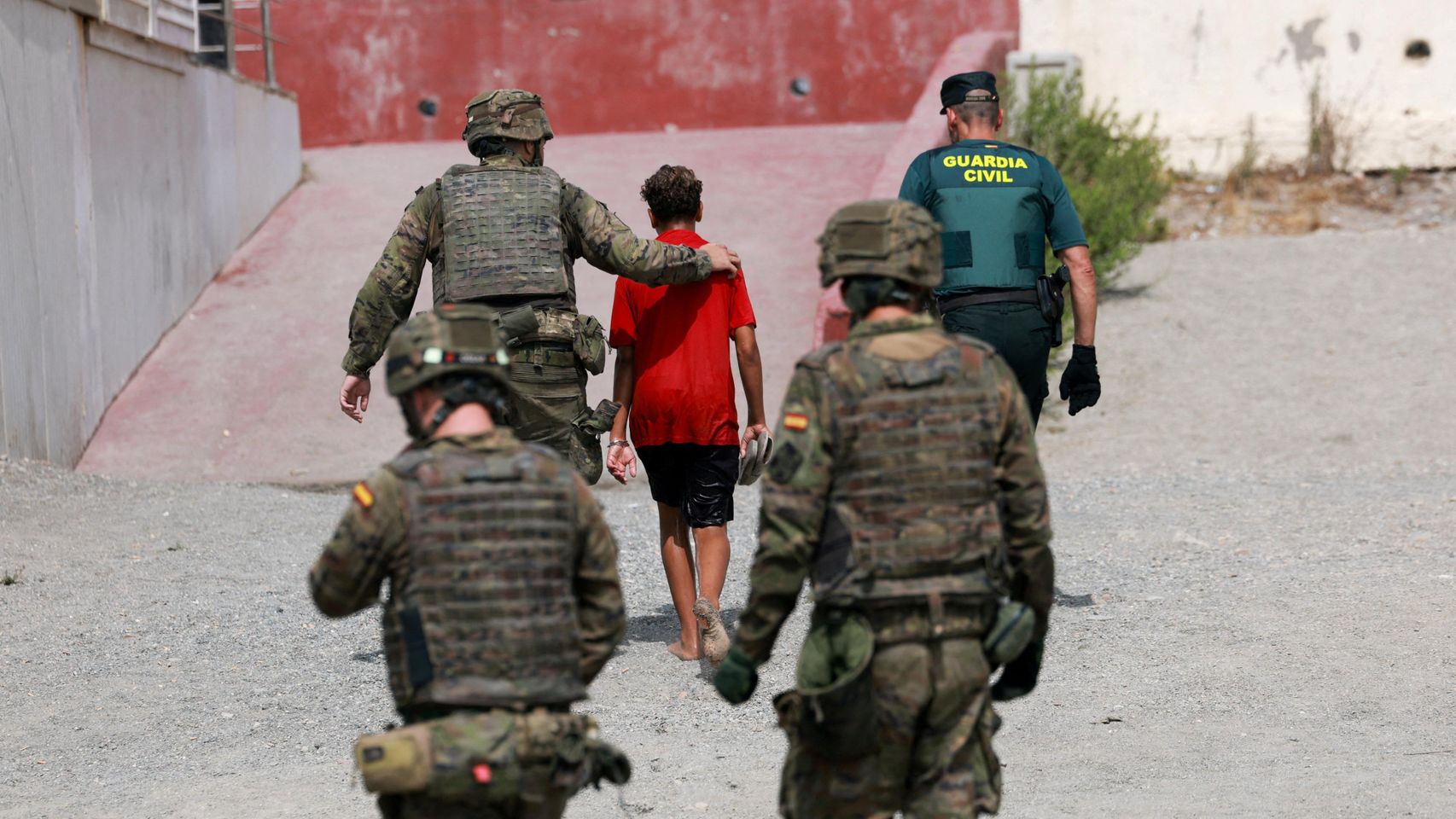 Cuerpos de seguridad junto a un menor migrante en Ceuta.