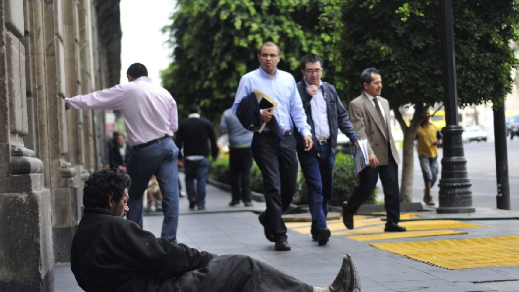 Un indigente tumbado en la calle bajo la mirada de los peatones.