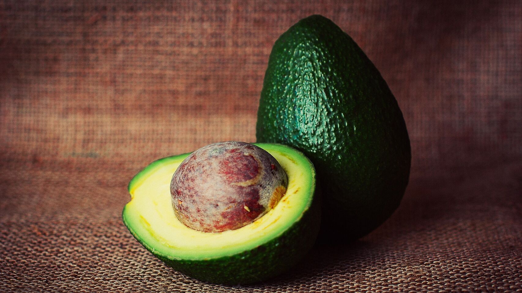 Un aguacate entero y otro cortado por la mitad.